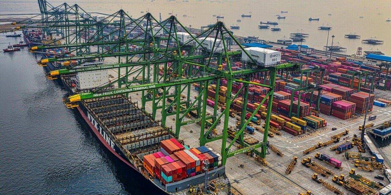 Aerial view of cargo containers being loaded on a ship that is docked on a busy port.