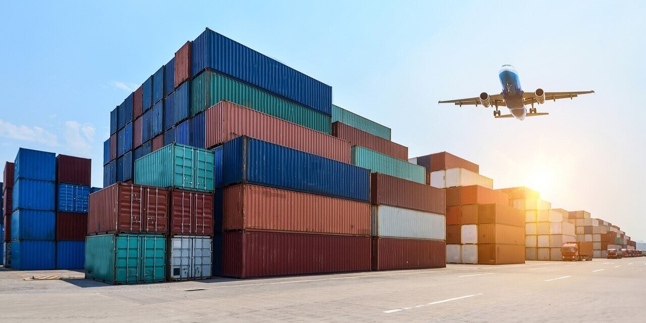 An aircraft navigates the sky above a container terminal, highlighting the dynamic nature of global shipping and logistics.
