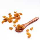 Dried raisins scattered on a plain background, along with a wooden spoon.
